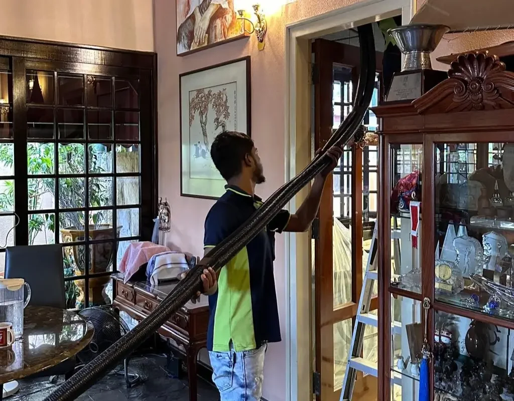 Technician connecting industrial vacuum hose to aircon PVC drainage pipe exit on Singapore HDB flat wall