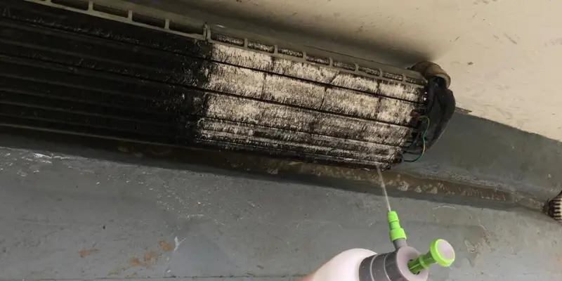 Aircon technician applying chemical wash solution to aluminum fan coil fins of a wall-mounted aircon unit in Singapore