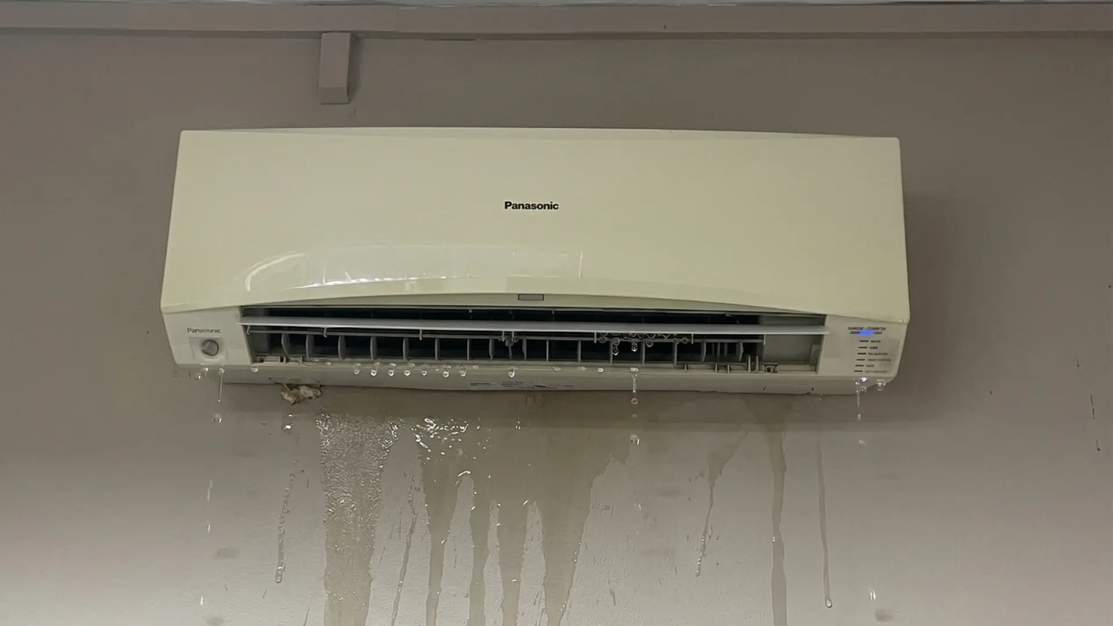 Wall-mounted aircon unit leaking water onto parquet floor in Singapore HDB bedroom at night