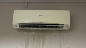 Wall-mounted aircon unit leaking water onto parquet floor in Singapore HDB bedroom at night