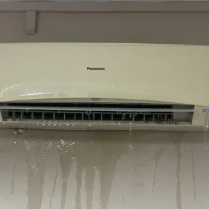 Wall-mounted aircon unit leaking water onto parquet floor in Singapore HDB bedroom at night