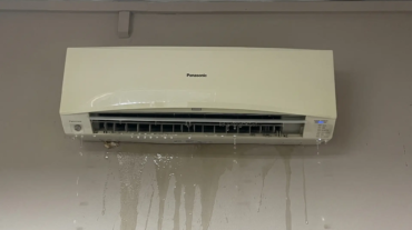Wall-mounted aircon unit leaking water onto parquet floor in Singapore HDB bedroom at night