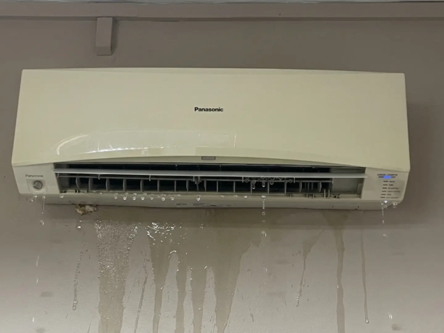 Wall-mounted aircon unit leaking water onto parquet floor in Singapore HDB bedroom at night