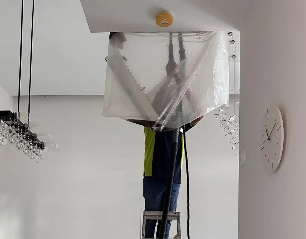 Aircon technician in navy uniform using industrial vacuum to clear blocked drainage pipe on Singapore HDB flat exterior