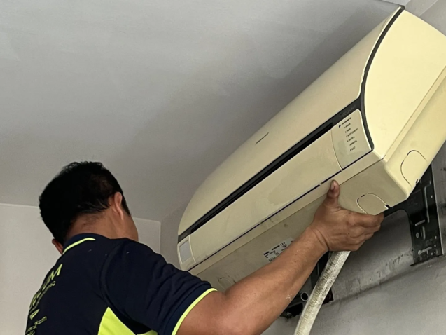 Professional technician relocating a split air conditioner inside a Singapore HDB flat.