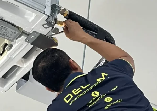 Close-up of a technician from Decom Aircon Services Singapore installing copper piping and insulation for a Mitsubishi Electric ceiling cassette air conditioner.